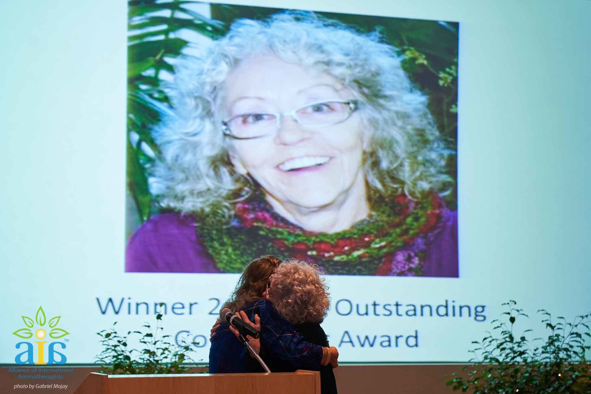 Sylla Recognized for Outstanding Contributions   At the Alliance of International Aromatherapists Conference this past August, many friends and colleagues had the pleasure of seeing Sylla win win this year's Outstanding Contributions Award. Thanks to our student's idea, we managed to get it on video. Check out our Facebook Live Video and see what it was like to be in the room during Sylla's second most happiest moment of her life. You'll also learn what her most happiest moment has been. Here is Sylla's response: I finally feel seen. I have worked 40 years in this field and accomplished a lot, and I feel like for the first time my story was told and I was honored for my efforts. When I started teaching long ago it was my dream to make a difference in the world of aromatherapy. As I went along and created Atlantic Institute of Aromatherapy, I had more ideas, wrote a book, hooked up with safety experts, went to Purdue and France chasing my dream and teaching others along the way.  After 9/11, I was moved to act, the UAE, Inc. formed organically and was supported by the community. Now the organization has been reinstated for the future generations! Getting the award and listening to the 11 mins of accomplishments was like a dream come true, I amazed myself(!) and felt completely recognized for the first time ever in my aroma career.  Watching the video later I realized there was this slideshow playing behind me, little did I know the care that Lora Cantele took to make the presentation. As the conference went on I learned how much some wanted me to win this, and how much they felt I deserved it long ago. I also learned that many did not even know all I have done in my 40 years. I feel completely seen and heard for the first time. With this honor, I feel that I leave a good legacy and hope to inspire others. I am so glad I was alive to say this! I have never felt so loved, honored and appreciated, in my life. I lovingly accept all the recognition and feel like my cup is overflowing again.   Thank you everyone who voted for Sylla. We hope to see you at the next Alliance of International Aromatherapists Conference in 2019!          